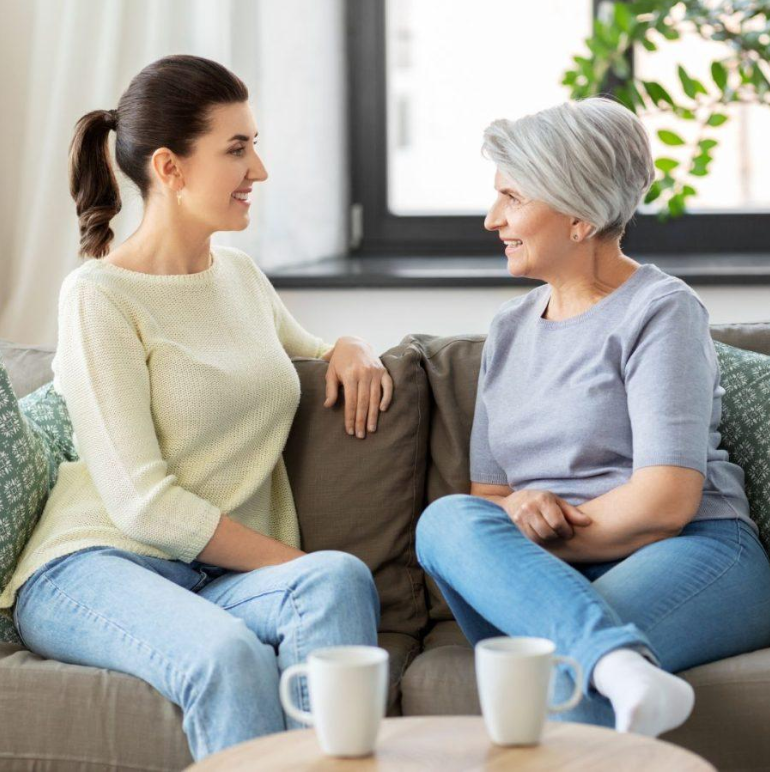 A younger woman sharing a relaxed conversation with an older woman at home